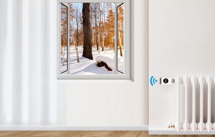 Termostatická hlavice MOES TRV 801 ZigBee na radiátoru v místnosti se zimní krajinou za oknem