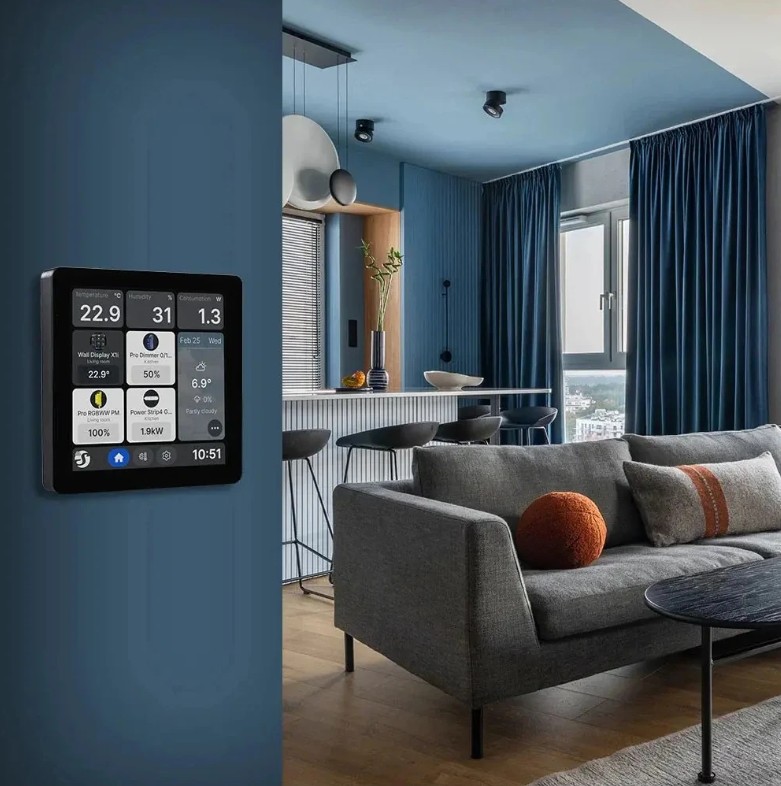 Shelly Wall Display X1i černý instalovaný na stěně v moderním obývacím pokoji. Na displeji jsou viditelné údaje o teplotě, vlhkosti, spotřebě, počasí a ovládací prvky chytré domácnosti.