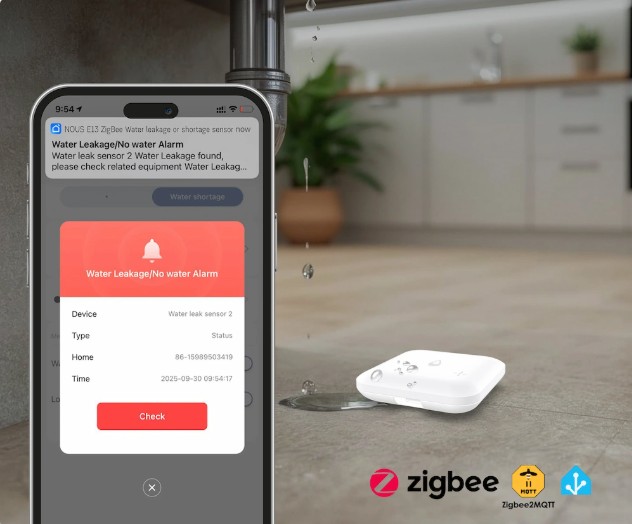 Mobilní telefon zobrazuje upozornění na únik vody, zatímco senzor NOUS E13 leží na podlaze vedle potrubí s unikající vodou.