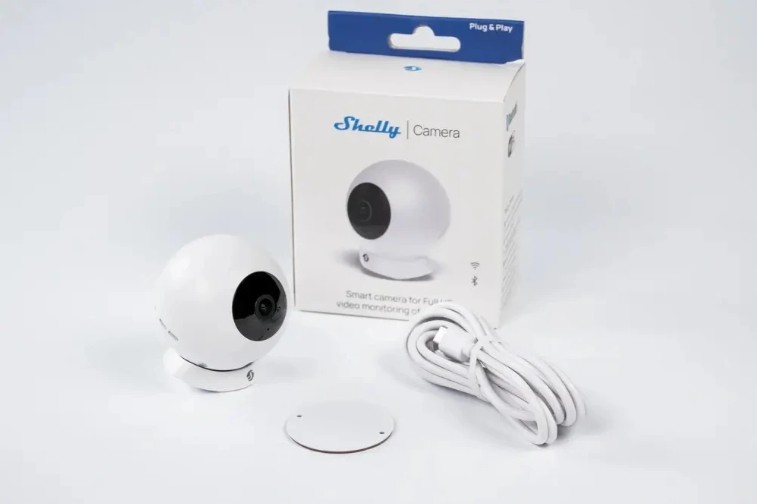 Bílá kamera Shelly Camera White se stojánkem, napájecím kabelem a balením produktu Shelly Camera na světlém pozadí