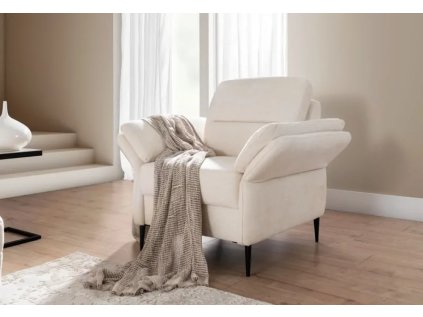 Křeslo WHISPER v interiéru, světlé křeslo u okna s dekou, šikmý pohled v moderní místnosti.