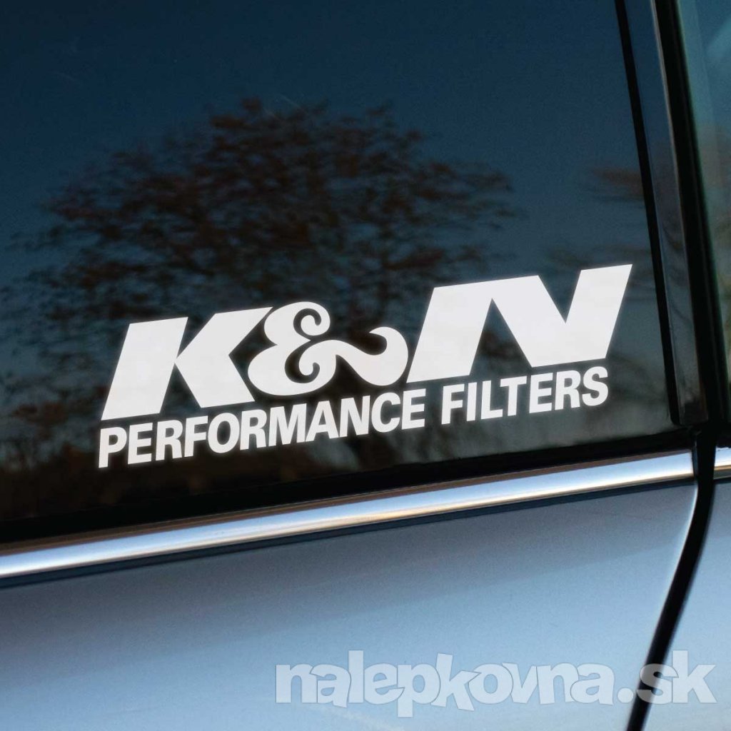 Biela nálepka "K&N Performance Filters" na zadnom okne elegantného strieborného auta. Nálepka zdôrazňuje výkonnostné filtre značky K&N, čo môže zvýšiť záujem o kvalitné autodoplnky. Ideálne pre fanúšikov automobilov, ktorí hľadajú nálepky na auto s dôrazom na výkon a štýl.