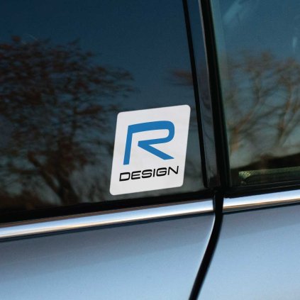 Tlačená nálepka „R DESIGN“ s modrým písmenom „R“ a moderným dizajnom na bielom podklade. Štýlový doplnok pre vozidlá Volvo R-Design.