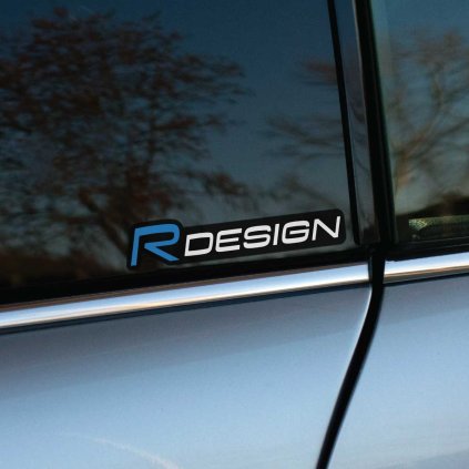 Tlačená nálepka „R DESIGN“ s elegantným čiernym podkladom a modrým písmenom „R“. Prémiový detail pre vozidlá Volvo R-Design.
