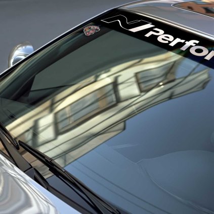 Sunstrip s veľkým vyrezaným nápisom N Performance v stredovej časti v detaile na čelnom skle strieborného BMW.