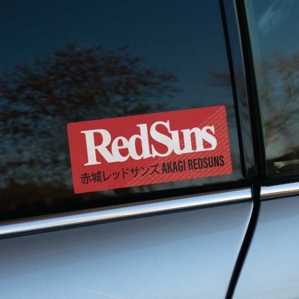 Tlačená nálepka „Red Suns Akagi Redsuns“ s výrazným logom a japonským textom, inšpirovaná legendárnym tímom z pouličných závodov.