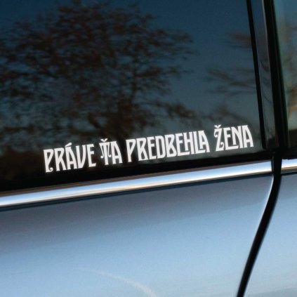 Plotrovaná nálepka na auto s textom „Práve ma predbehla žena“ v úzkom retro štýle pre decentné, no sebavedomé vyjadrenie.