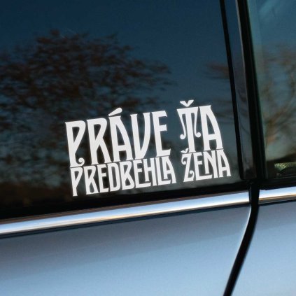 Plotrovaná nálepka s ozdobným pätkovým písmom v dvoch riadkoch a s nápisom: PRÁVE ŤA PREDBEHLA ŽENA. Vyrezávaný motív.