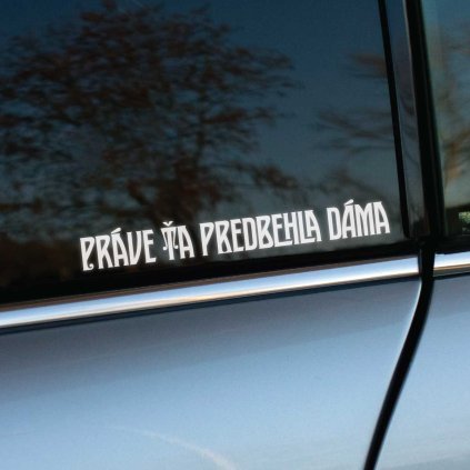 Plotrovaná nálepka s ozdobným pätkovým písmom a vodorovným rozložením, text: PRÁVE ŤA PREDBEHLA DÁMA. Vyrezávaný motív.