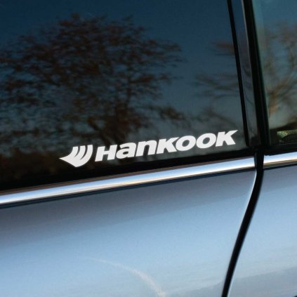 Biela nálepka s logom "Hankook" a charakteristickým grafickým prvkom umiestnená na zadnom okne automobilu. Táto nálepka je ideálnym spôsobom, ako vyjadriť podporu jednej z popredných značiek pneumatík a dodať autu dynamický vzhľad. Jednoduchý a čistý dizajn vyniká na tmavom skle, čo ju robí perfektným doplnkom pre každého automobilového nadšenca.  **Kľúčové slová:** nálepka na auto Hankook, nálepky na okno auta, reklamné nálepky Hankook, tuningové nálepky, polepy na auto, nálepky na podporu značky pneumatík, značkové nálepky na auto, kvalitné nálepky na auto, dizajnové auto nálepky, doplnky na auto Hankook.