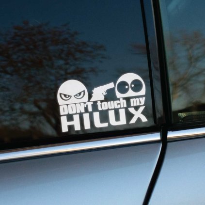 Plotrovaná nálepka s textom „Don’t touch my Hilux“, zamračená tvár so zbraňou mieri na prekvapenú tvár.