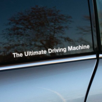 Plotrovaná nálepka na auto s textom The Ultimate Driving Machine, decentný a elegantný detail pre priaznivcov značky BMW.