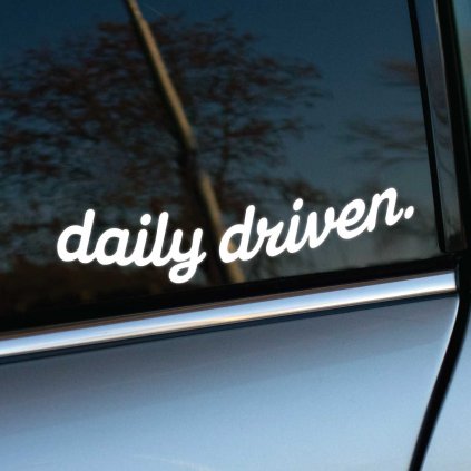 Biela nálepka s nápisom "daily driven." umiestnená na bočnom okne strieborného auta. Jednoduchý, ale výrazný dizajn nálepky symbolizuje, že vozidlo je pravidelne využívané, čím podčiarkuje jeho každodennú spoľahlivosť. Skvelý doplnok pre každodenných vodičov, ktorí chcú dodať svojmu autu osobný a štýlový detail.