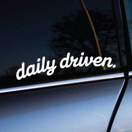 Biela nálepka s nápisom "daily driven." nalepená na bočnom okne tmavosivého auta. Tento jednoduchý, no výstižný dizajn nálepky vyjadruje, že auto je každodenne používané, čo pridáva osobitý charakter a štýl vozidlu. Ideálna voľba pre tých, ktorí chcú ozdobiť svoje auto s dôrazom na jeho praktickosť a pravidelné používanie.