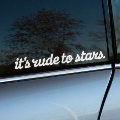 Nálepka na aute s nápisom "it's rude to stars" v bielom písme je nalepená na tmavom okne dverí. Okno odráža vonkajšie prostredie, čo vytvára zaujímavý kontrast medzi jemným textom a okolitou prírodou. Perfektný doplnok pre milovníkov originality a kreatívnych citátov na vozidle. Táto nálepka zaujme na prvý pohľad a dodáva autu jedinečný charakter.