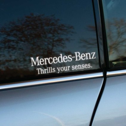 Na fotografii je detail okna auta Mercedes-Benz, na ktorom je nalepená nálepka s textom "Mercedes-Benz Thrills your senses." Táto nálepka bez loga značky, ale s výrazným sloganom, dodáva vozidlu sofistikovaný vzhľad a podčiarkuje emocionálny zážitok z jazdy, ktorý táto značka ponúka. Biela farba textu na tmavom pozadí okna vytvára elegantný kontrast, ktorý je ideálny pre každého majiteľa Mercedesu, ktorý chce svojmu autu dodať jedinečný a prémiový dotyk.