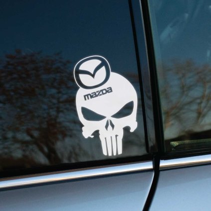Na fotografii je automobil značky Mazda, na ktorom je nalepená biela nálepka s motívom lebky inšpirovanej postavou The Punisher, doplnená o logo Mazda. Táto nálepka dodáva autu odvážny a výrazný vzhľad, čo osloví majiteľov vozidiel Mazda, ktorí chcú svojmu vozidlu pridať štipku osobitosti a zvýrazniť jeho športový charakter. Perfektný doplnok pre tých, ktorí hľadajú originálne a výrazné dekorácie pre svoje auto.