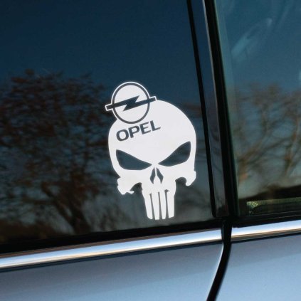 Na fotke je detail boku automobilu značky Opel, na ktorom je nalepená biela nálepka s dizajnom lebky v štýle The Punisher, doplnená logom Opel. Táto nálepka pridáva autu výrazný a drsný vzhľad, vhodný pre všetkých fanúšikov značky Opel, ktorí chcú zvýrazniť svoj vkus a štýl. Ideálna dekorácia na zadné sklo auta, ktorá okamžite pritiahne pozornosť.
