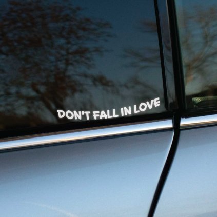Plotrovaná nálepka Don't Fall In Love s jednoduchým textom v miernom oblúku, decentná voľba s jemným odkazom.