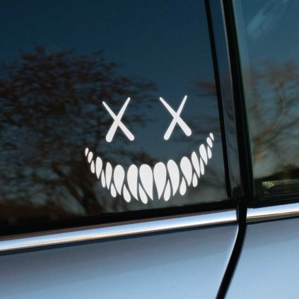 Plotrovaná nálepka na auto s preškrtnutými očami a širokým úsmevom plným špicatých zubov v štýle temného smajlíka.