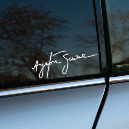 Plotrovaná nálepka s autentickým podpisom Ayrtona Sennu v elegantnom písanom štýle s plynulými líniami a dynamickým charakterom písma.