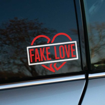 Plotrovaná nálepka na auto so zlomeným srdcom a výrazným nápisom „FAKE LOVE“ v šikmom obdĺžnikovom rámčeku.