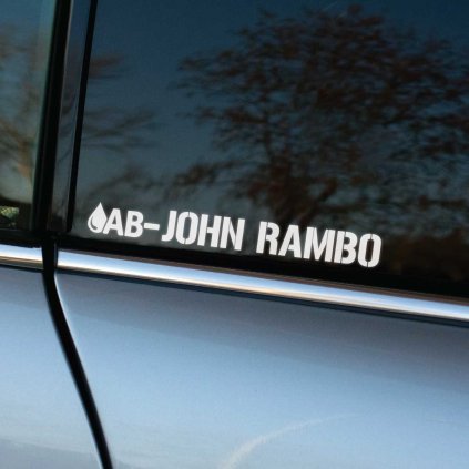 Plotrovaná nálepka na auto s menom „John Rambo“ a kvapkou krvi s krvným typom AB− v robustnom vojenskom písme.
