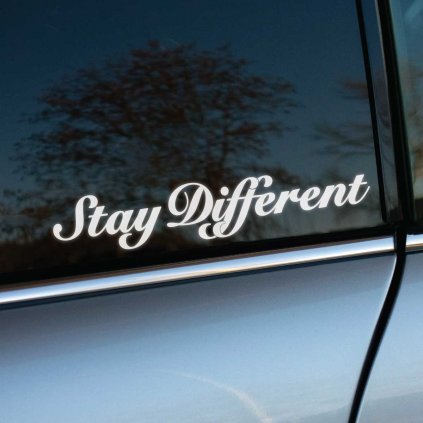 Detailný záber na okno auta s bielou nálepkou "Stay Different" v elegantnom písme. Nálepka je umiestnená na zadnom bočnom okne a vyniká na tmavom pozadí, čo zdôrazňuje jej štýlový a jedinečný dizajn. Perfektný doplnok pre automobilových nadšencov, ktorí chcú vyjadriť svoju individualitu a odlišnosť od ostatných.