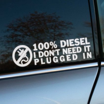 Nálepka na bočnom okne auta s textom "100% DIESEL I DON'T NEED IT PLUGGED IN" v bielom písme, nad ktorým je ikona zástrčky s prečiarknutím, symbolizujúca nezávislosť na elektrickej energii, na pozadí s odrazom stromov a neba.