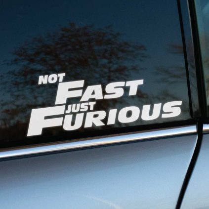 Fotografia zobrazuje bočné okno auta so samolepkou, na ktorej je bielym písmom napísané "NOT FAST JUST FURIOUS". Tento nápis s humorom naznačuje, že vozidlo nemusí byť najrýchlejšie, ale jeho vodič je určite vášnivý a energický.