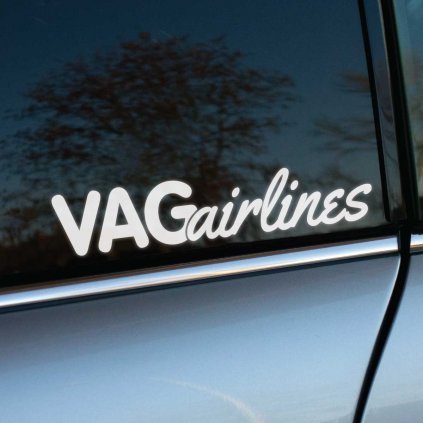 Fotografia zobrazuje nálepku s nápisom "VAGairlines", ktorá je nalepená na bočnom okne auta. Nálepka je bielej farby a text je napísaný kombináciou veľkých a malých písmen, kde "VAG" je veľkými písmenami a "airlines" je napísané kurzívou malými písmenami. Nálepka výrazne kontrastuje s tmavým sklom okna auta. V pozadí sú viditeľné stromy a modrá obloha, ktoré sa odrážajú na skle. Fotografia je pravdepodobne urobená vonku za denného svetla.