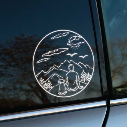 Plotrovaná nálepka kruhového tvaru s motívom osoby a psa sediacich pred horami, stromami a oblohou, ideálna na okno auta.