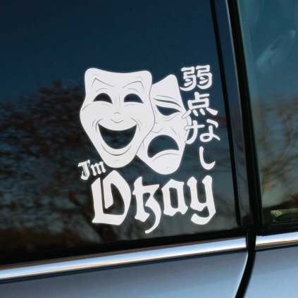 Plotrovaná nálepka I’m Okay s divadelnými maskami a japonským nápisom, silný kontrast medzi emóciami a textom.