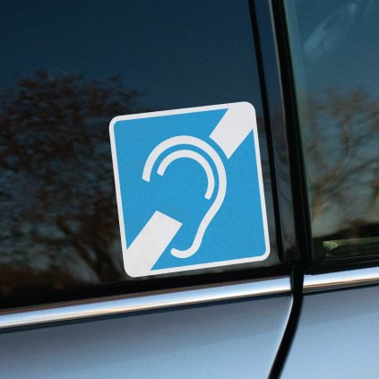 Tlačená nálepka s modrým symbolom ucha a preškrtnutím, určená na označenie vozidiel pre osoby so sluchovým postihnutím.
