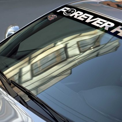 Sunstrip s veľkým bielym nápisom FOREVER v stredovej časti v detaile na čelnom skle strieborného vozidla značky BMW.