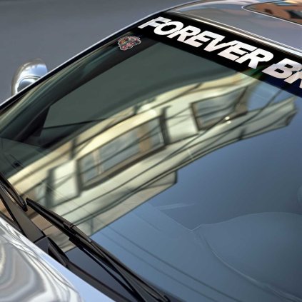 Sunstrip s veľkým bielym nápisom FOREVER BR v stredovej časti v detaile na čelnom skle strieborného vozidla BMW.