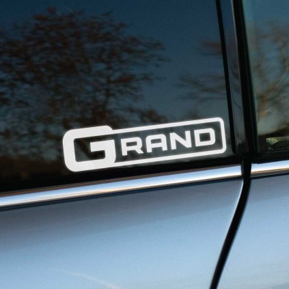 Plotrovaná nálepka s nápisom „GRAND“ v dynamickom ráme. Moderný doplnok pre zvýraznenie modelu SsangYong Musso Grand.
