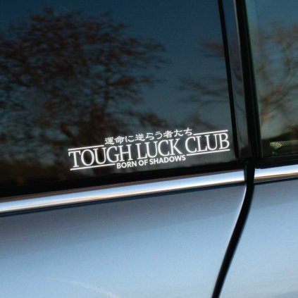 Plotrovaná nálepka s nápisom TOUGH LUCK CLUB, doplnená japonským textom a sloganom BORN OF SHADOWS v temne ladenom štýle.
