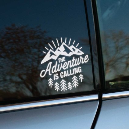 Plotrovaná nálepka na auto s motívom hôr, stromov a textom „The adventure is calling“ v dobrodružnom outdoor štýle.