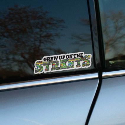 Tlačená nálepka na auto s nápisom „Grew up on the streets“ a výplňou z detského koberca s motívom ciest a budov.