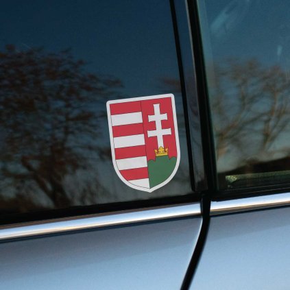 Tlačená nálepka s maďarským erbom, ľavá polovica s červenobielymi pruhmi, pravá s dvojkrížom nad zelenými vrchmi a zlatou korunou.
