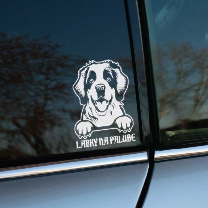 Plotrovaná nálepka na auto s motívom rozosmiateho bernardína. Pes má labky položené na spodnej hrane okna. Pod ním je text „LABKY NA PALUBE“.