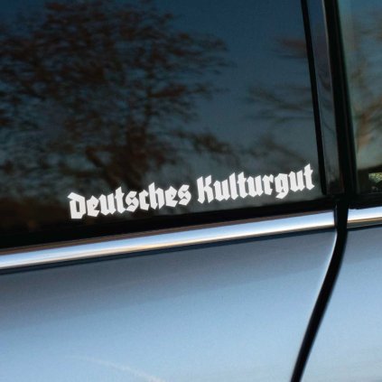 Plotrovaná nálepka Deutsches Kulturgut. Vyrezávaný nápis v tradičnom gotickom písme s ozdobnými hranatými prvkami a líniami.