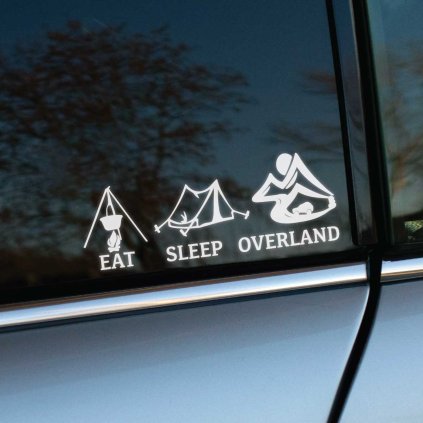 Plotrovaná nálepka EAT SLEEP OVERLAND, vyrezávaný motív kotlíka nad ohňom, stanu a terénneho auta v horách s anglickým textom.