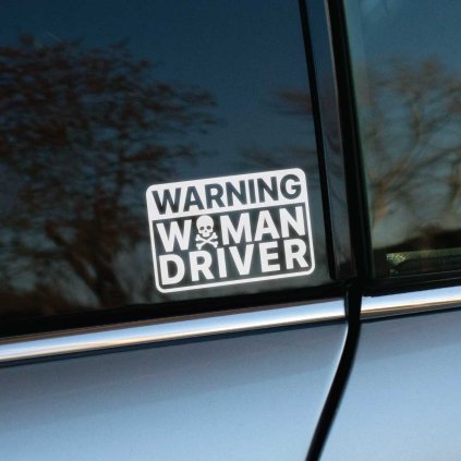 Plotrovaná nálepka, obdĺžnikový rám, motív lebky s hnátmi a trojriadkový text: WARNING WOMAN DRIVER. Vyrezávaný tvar.