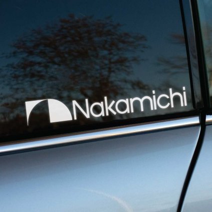 Biela nálepka „Nakamichi“ na okne auta s moderným a minimalistickým dizajnom, ktorý zvýrazňuje logo známej značky. Nálepka je nalepená na tmavom skle a vyniká svojou kontrastnou bielou farbou, čo je ideálne pre zviditeľnenie na vozidlách. Tmavomodrá karoséria auta spolu s nálepkou vytvára elegantný a profesionálny vzhľad. Táto nálepka je perfektná voľba pre milovníkov áut, ktorí chcú personalizovať svoje vozidlo štýlovým doplnkom. Kľúčové slová: nálepky na auto, dizajnové nálepky, moderné logo, personalizácia vozidla.