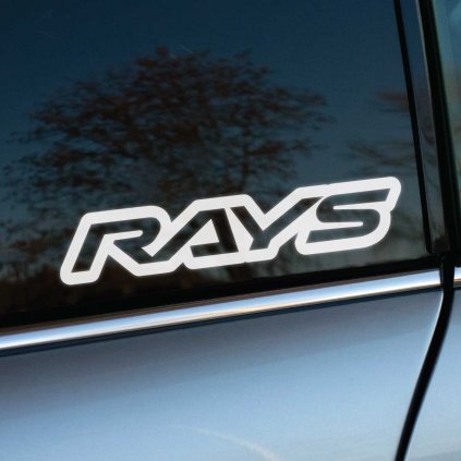 Biela nálepka „Rays“ s moderným a dynamickým písmom je nalepená na zadnom bočnom okne auta. Tento štýlový dizajn reprezentuje prémiovú značku kolies známych svojou kvalitou a výkonom, pričom na tmavom skle vyniká ostrým kontrastom. Ideálna voľba pre automobilových nadšencov, ktorí chcú zdôrazniť športový charakter svojho vozidla a vášeň pre špičkové technológie v oblasti kolies. Perfektný doplnok pre tuningové a pretekárske autá.