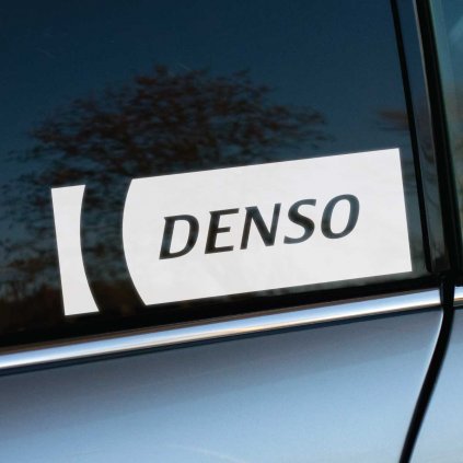 Biela nálepka „Denso“ s čistým a moderným dizajnom nalepená na tmavom bočnom okne auta. Logo je orámované výrazným grafickým prvkom, ktorý zvyšuje jeho viditeľnosť a dodáva nálepke profesionálny vzhľad. Kontrast medzi tmavým sklom a bielou nálepkou zvýrazňuje značku, zatiaľ čo strieborná karoséria auta dotvára sofistikovaný celok. Táto nálepka je ideálna pre motoristov a tuning nadšencov, ktorí chcú podporiť renomovaného výrobcu automobilových dielov. Kľúčové slová: nálepka Denso, auto nálepky, dizajnové nálepky, personalizácia auta, tuningové doplnky.