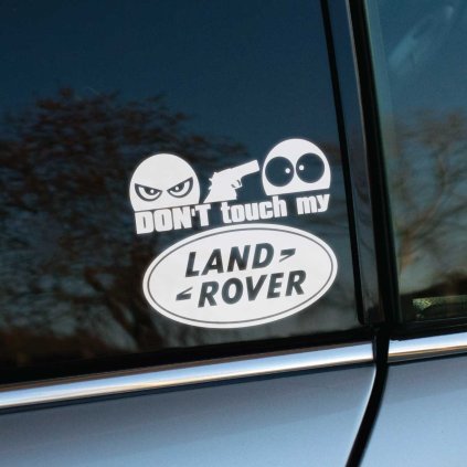 Plotrovaná nálepka s textom „Don't touch my Land Rover“, zamračená tvár so zbraňou mieri na prekvapenú tvár.