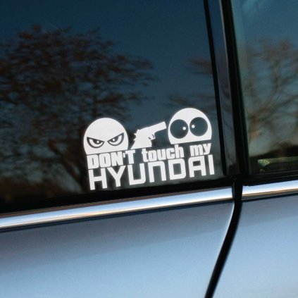 Plotrovaná nálepka s textom „Don’t touch my Hyundai“, zamračená tvár so zbraňou mieri na prekvapenú tvár.